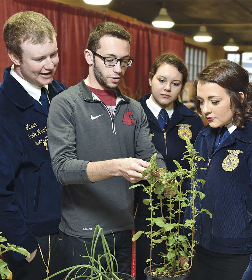 A college student explaining the parts of a plant to three FFA students