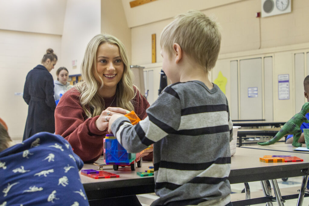 A college student playing magnet tiles with a child 