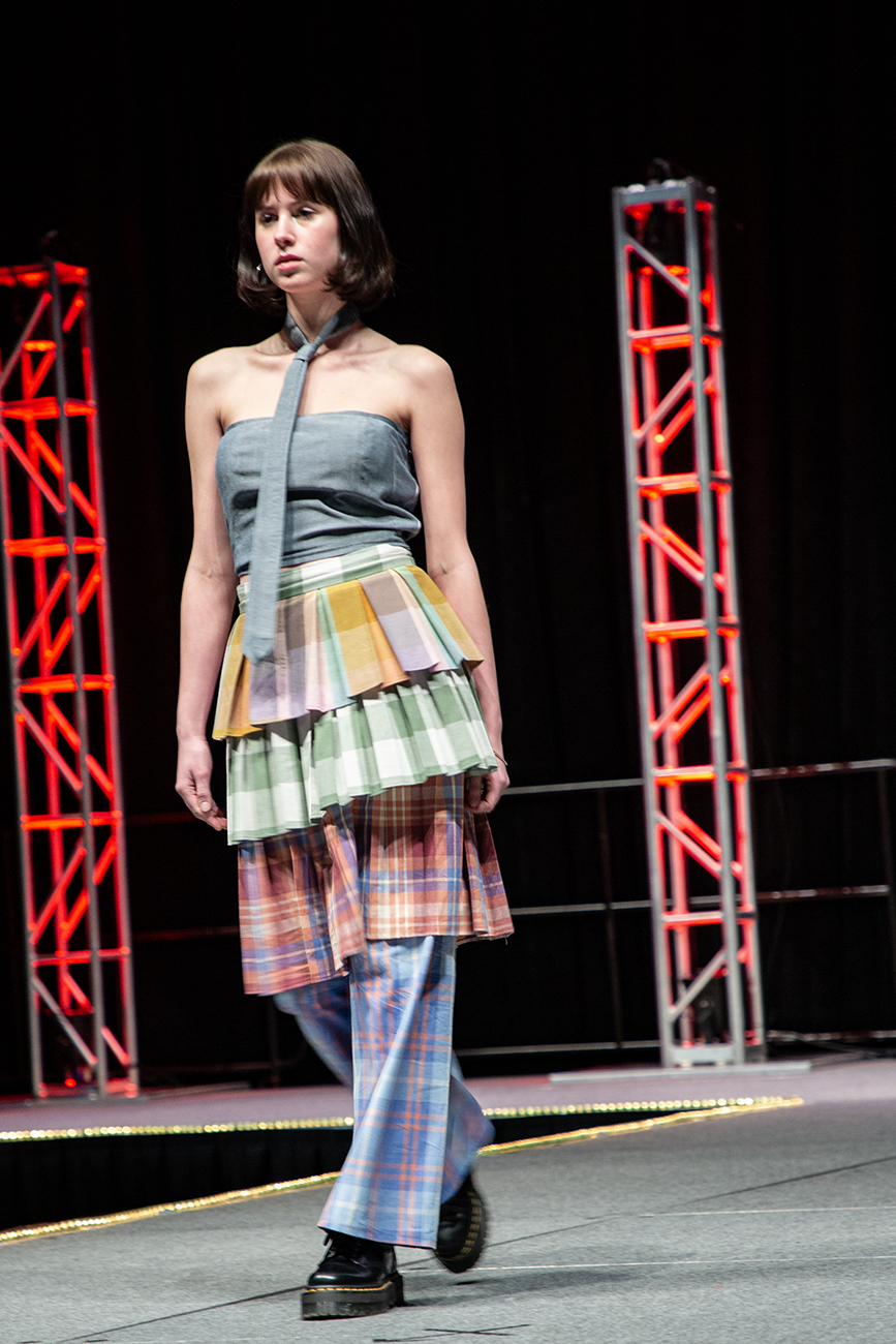 A model walking down teh runway with layers of plaid on, and a tie on