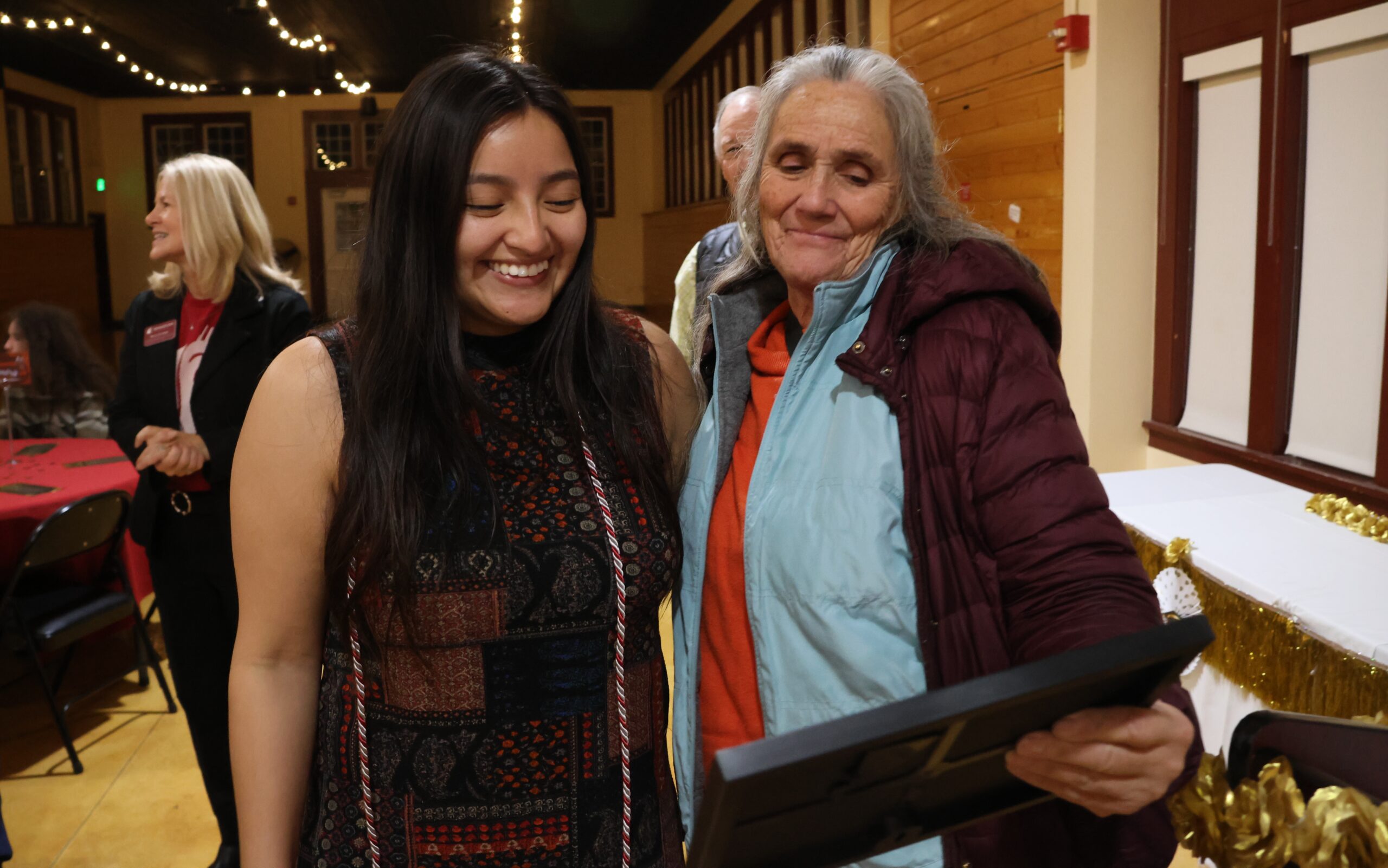 A dean's honor roll student wearing their honor chord and their parent look down at the student's certificate fondly.
