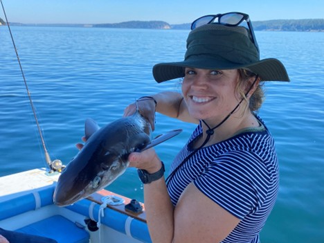 A person on a boat holds up a small shark up, the blue water behind her.