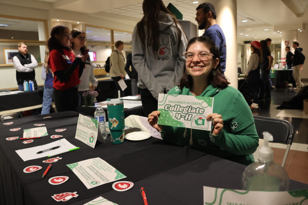 A 4-H student holds up a Collegiate 4-H sign at a booth at CAHNRS Career Night