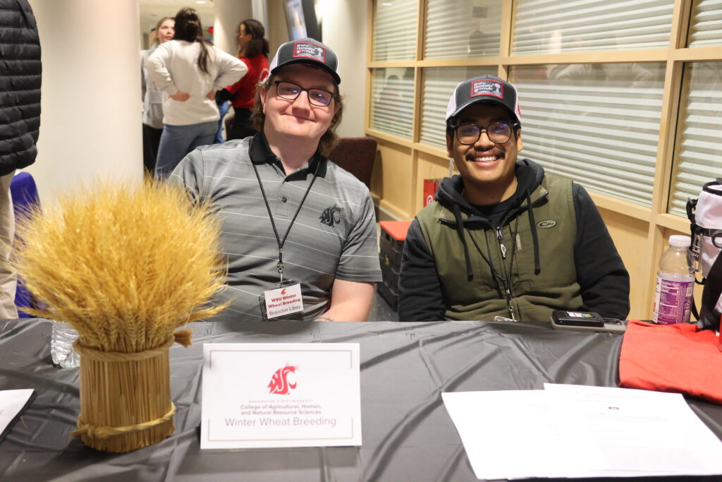 Two representatives of WSU Winter Wheat Breeding welcome folks with a tuft of wheat and big smiles.