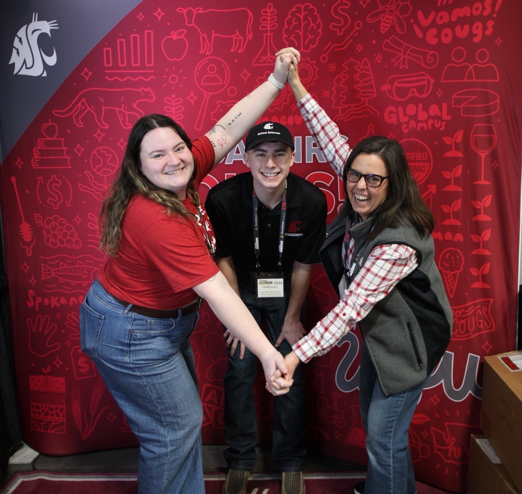 Three people pose make a silly diamond-shaped pose with their arms in front of an official CAHNRS backdrop.