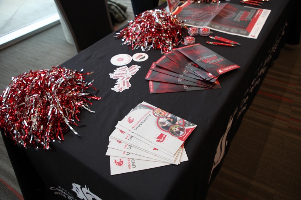 Brochures, stickers, and sparkly WSU pom-poms are laid out on a table.