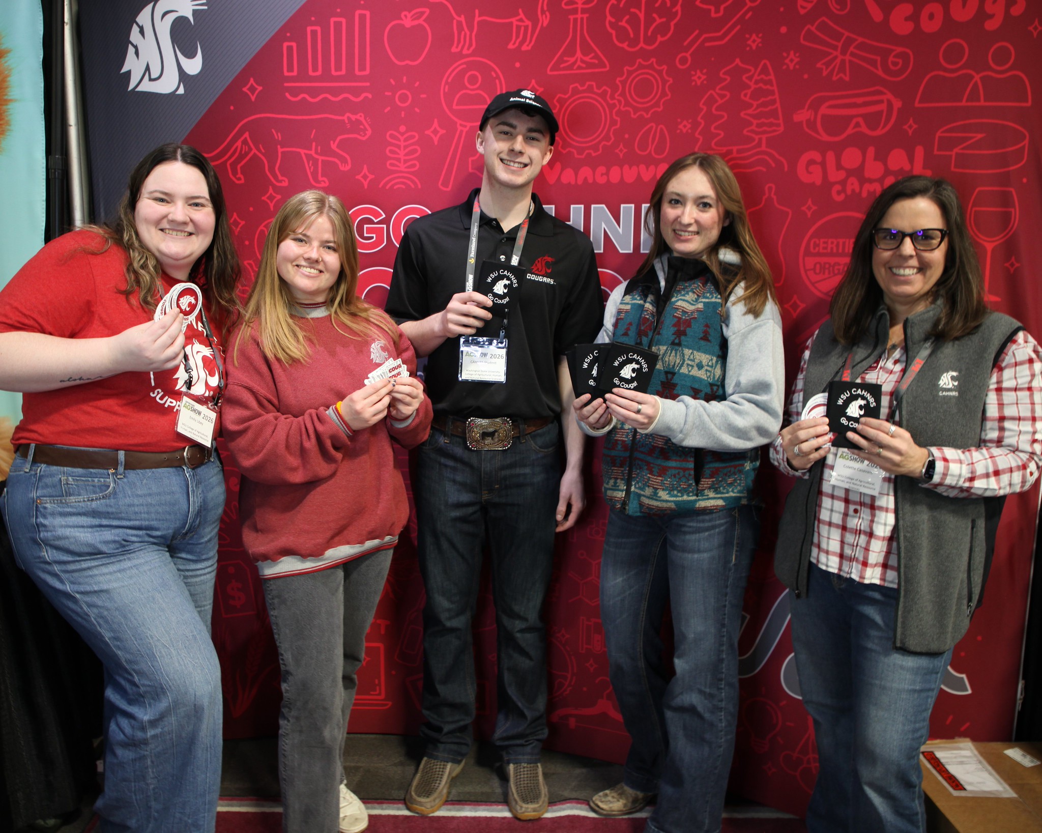 Group of 5 people holding CAHNRS stickers and swag in front of a WSU banner..