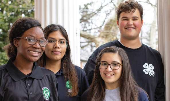 Four youth participants wearing 4-H shirts smiling outdoors
