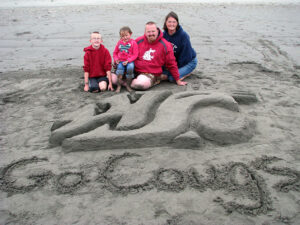 Future Cougs Wesley and Tessa Hausken with Dad, Eric (’01, Ag. Technol. & Prod. Mgmt.), and Mom, Sara (’03, Human Dev., ’07, Ed.), enjoy a day at the beach, where Eric created sand art honoring his alma mater.