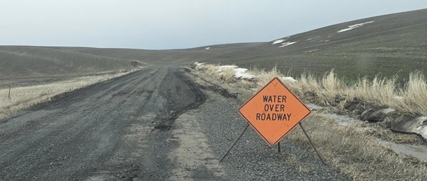 Gravel road on the Palouse with a Water Over Roadway sign in early spring.