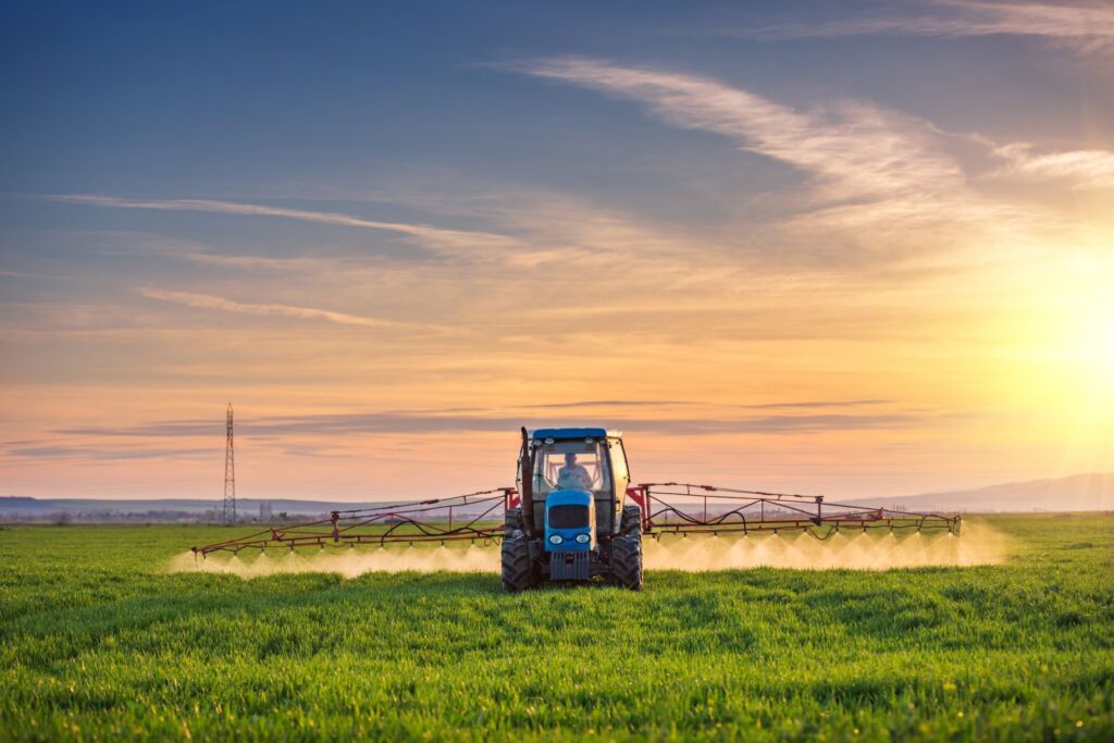 Tractor spraying fertilizer on green agriculture field.