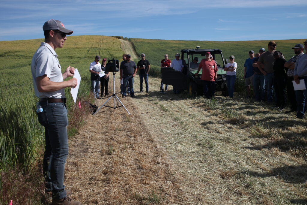 Field day attendees surrounding Morgan Menaker as he discusses wheat research at the Wike Field Day.