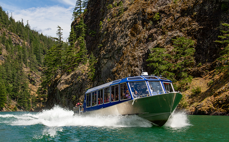 Boat riding through Diablo Lake, with blue green waters and large wake