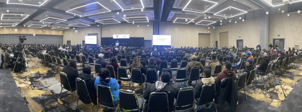 Panoramic view of large room of people with one speaker in the background presenting