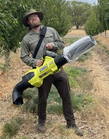 Man in orchard holding an electric leaf vacuum used to collect insects