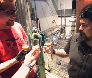 Caleb and another man hold tiny glasses with small amounts of beer.