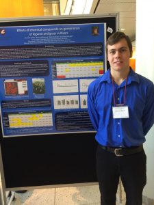 Brennan stands in front of his research poster, hanging from a board.
