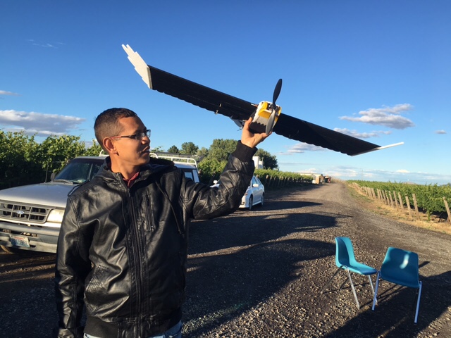 Precision-ag researcher Manoj Karkee holds up a flying drone in a vineyard.