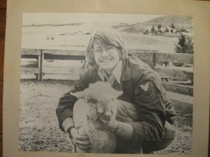 An old black and white photo of Mike Hacket crouched down with his arms around a sheep.