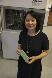 Holding a strip of green cloth, Hang Liu demonstrates use of a large piece of advanced lab equipment.