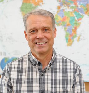 Head and shoulders photo of Kawula in front of world map