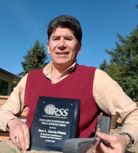 Dr. García-Pabón, seated outdoors, holding his award.
