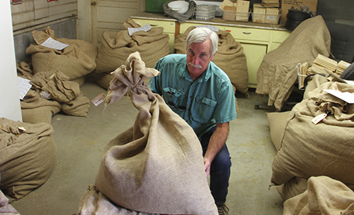 Walsh, holding a large burlap sack of hops, in a sack-filled workroom.