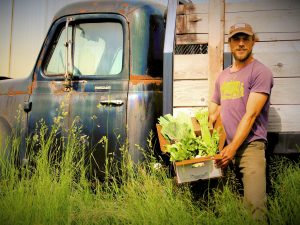Farmer holding a box of produce in front of an antique farm truck.