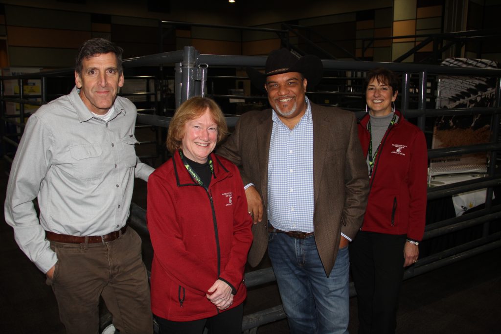 Group photo of college leaders and researchers, standing in front of a corrall on a convention room floor.