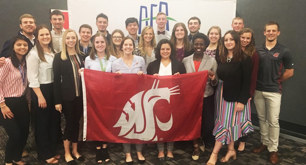 Group photo showing 21 students holding the Cougar flag at the AFA conference, with AFA banner in background.