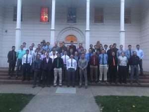 A group photo of the fraternity members standing outside their house.