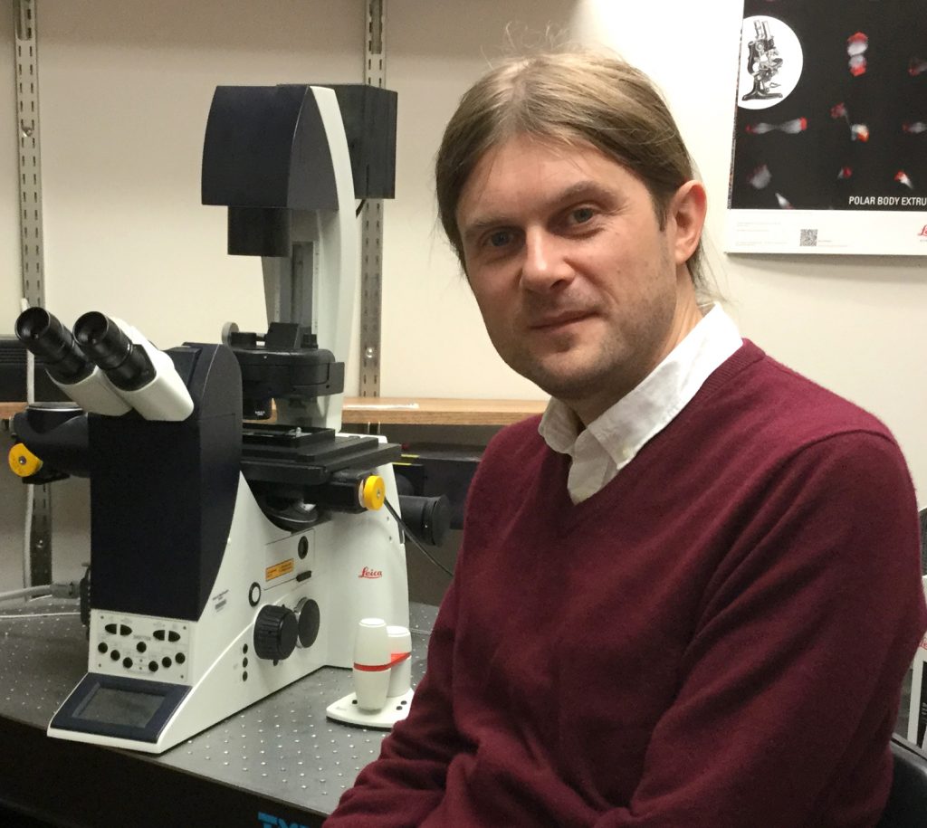 Smertenko, seated, in a lab with a microscope behind him.