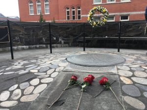 View of bronze plaque amid a stone memorial, with roses placed on the monument.