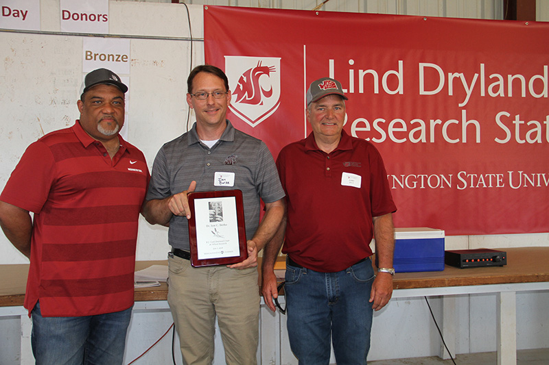 Burke, flanked by Wright and Bailey, in front of Lind banner. Burke holds plaque.