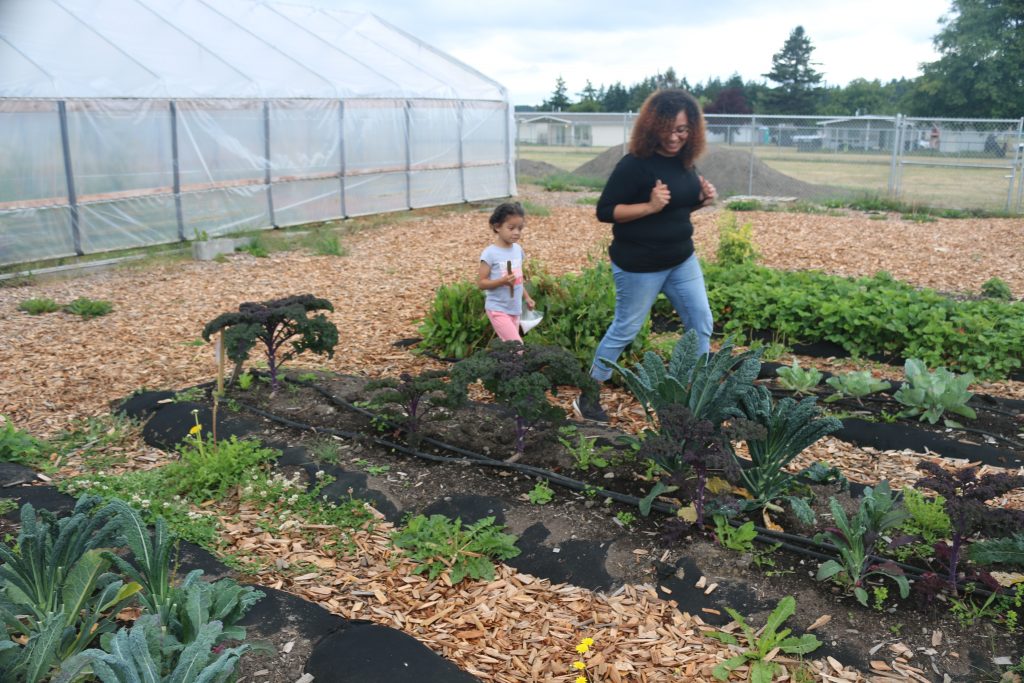 A woman and child walk in a garden with greenhouse in the background.