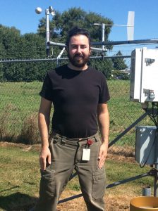 Contezac poses in front of a weather station, that includes a wind speed indicator and other electronic equipment.