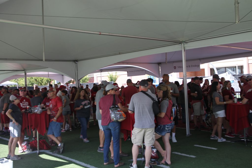 A couple of dozen people stand around under a white tent roof.