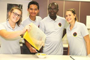 Group making porridge, pouring plastic packet into bowl.