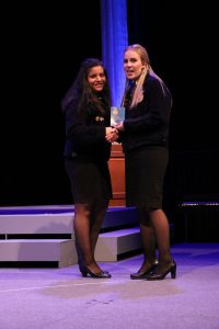 Arroyo-Mejia stands on a stage in an FFA jacket holding a plaque with another woman.