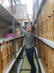 Murray reaches up high to pull a wooden rectangle of the top shelf, lined with many other rectangles.