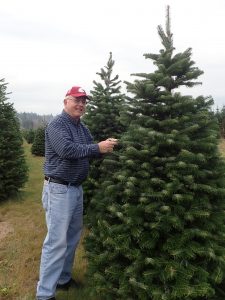 Chastagner stands next to a fir tree, looking at the camera and touching a few needles.