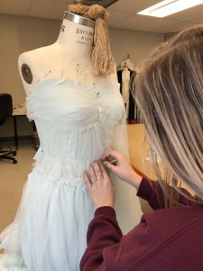 A blonde woman pinning fabric onto a dress.
