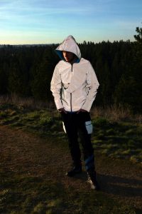 A young man in a white athletic jacket standing on the green grass.
