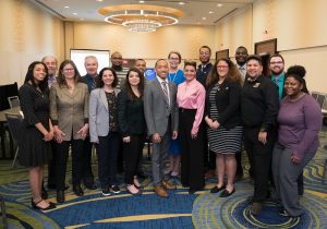 Large group of people in formal clothes in a large room.