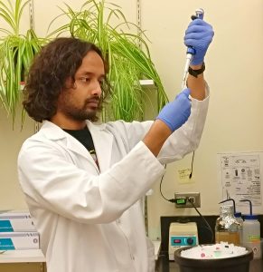 A young man wears a lab coat and gloves and he conducts a science experiment.