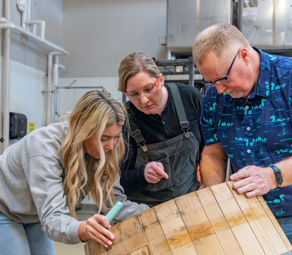 Two students and a faculty member working on a tipped wooden wine barrel in the Wine Science Center.