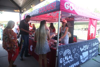 A few festivalgoers stand in front of a WSU CAHNRS-themed tent. Another person stands under the tent and hands a cup of ice cream to one of the people. Several other people stand in the background.