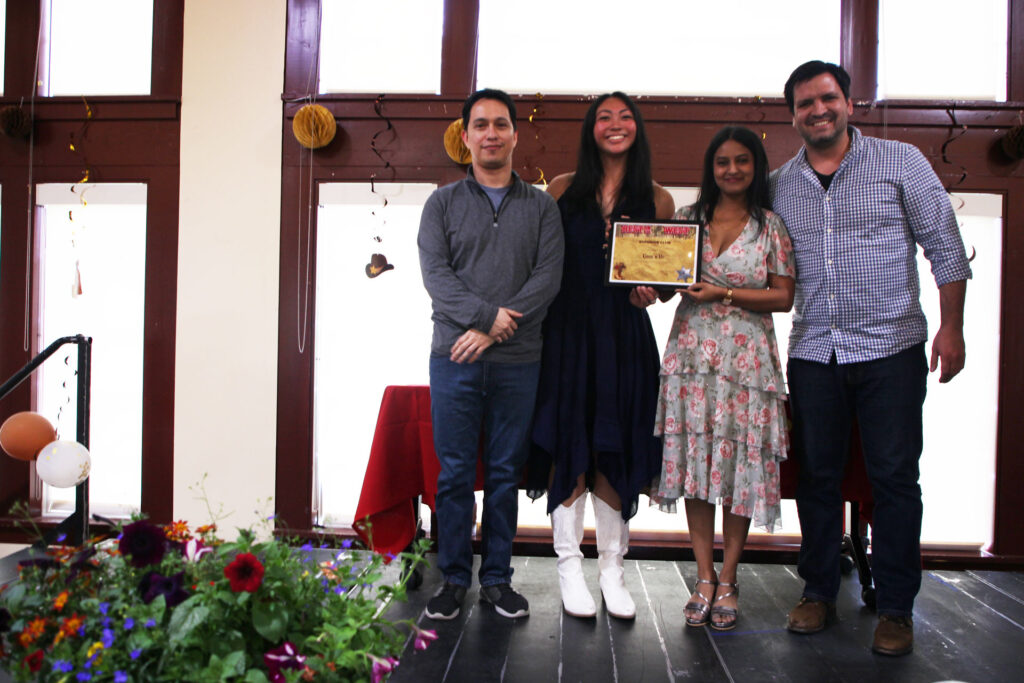 Four people stand together on a stage, holding a framed award.