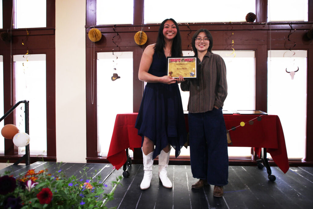 Two people stand together on a stage holding a framed award.