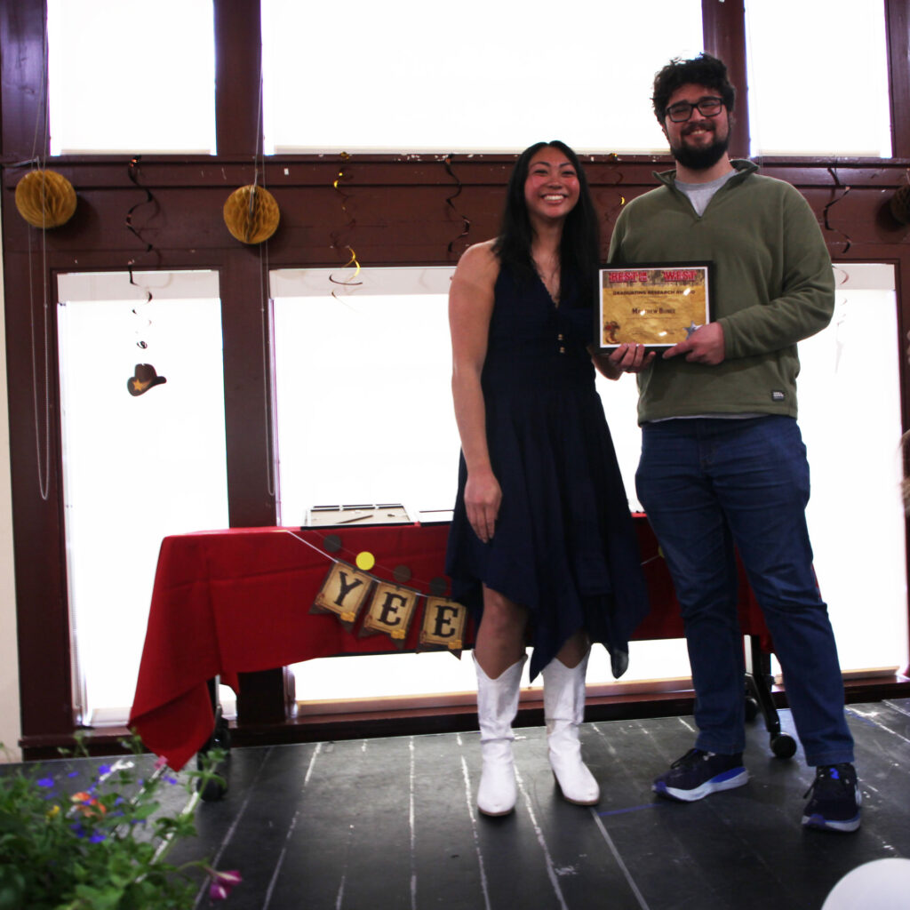Two people stand together on a stage holding a framed award.