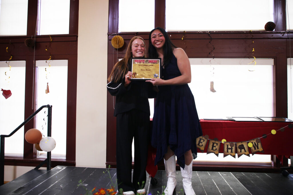 Two people stand together on a stage holding a framed award.
